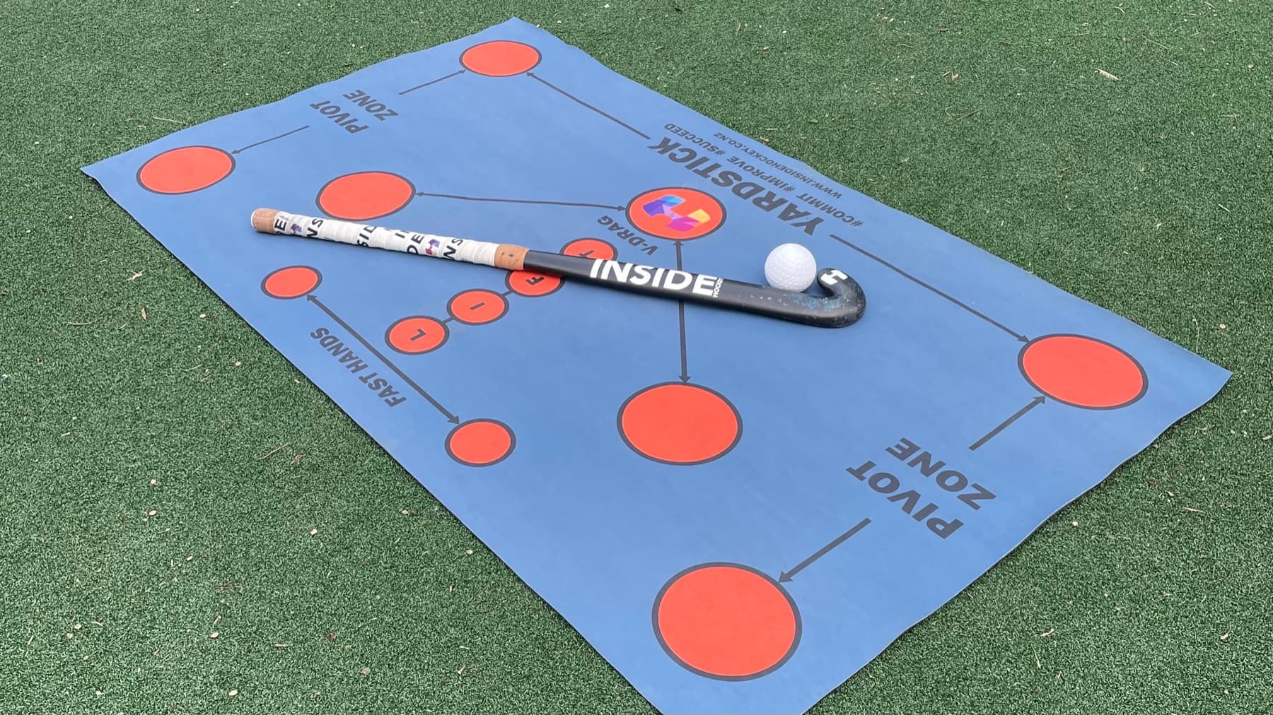 The Inside Hockey Skills Mat laid out on hockey turf with a stick and ball.