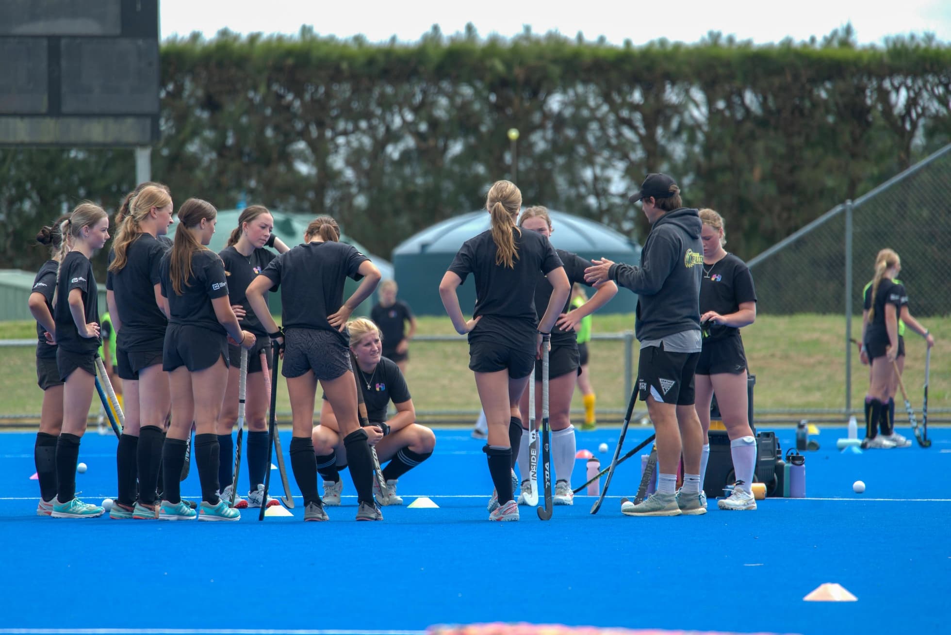 An Inside Hockey coach addressing a group of Camp players on blue turf.